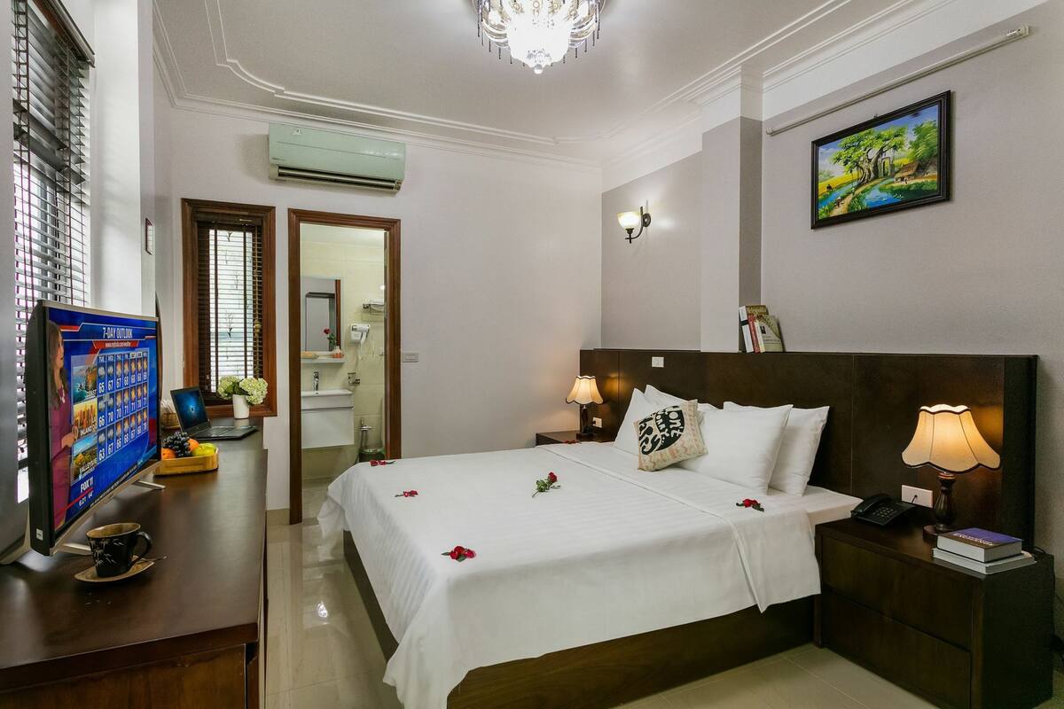 Quarto de hotel com uma cama grande, abajures, uma mesa com um computador e uma televisão.