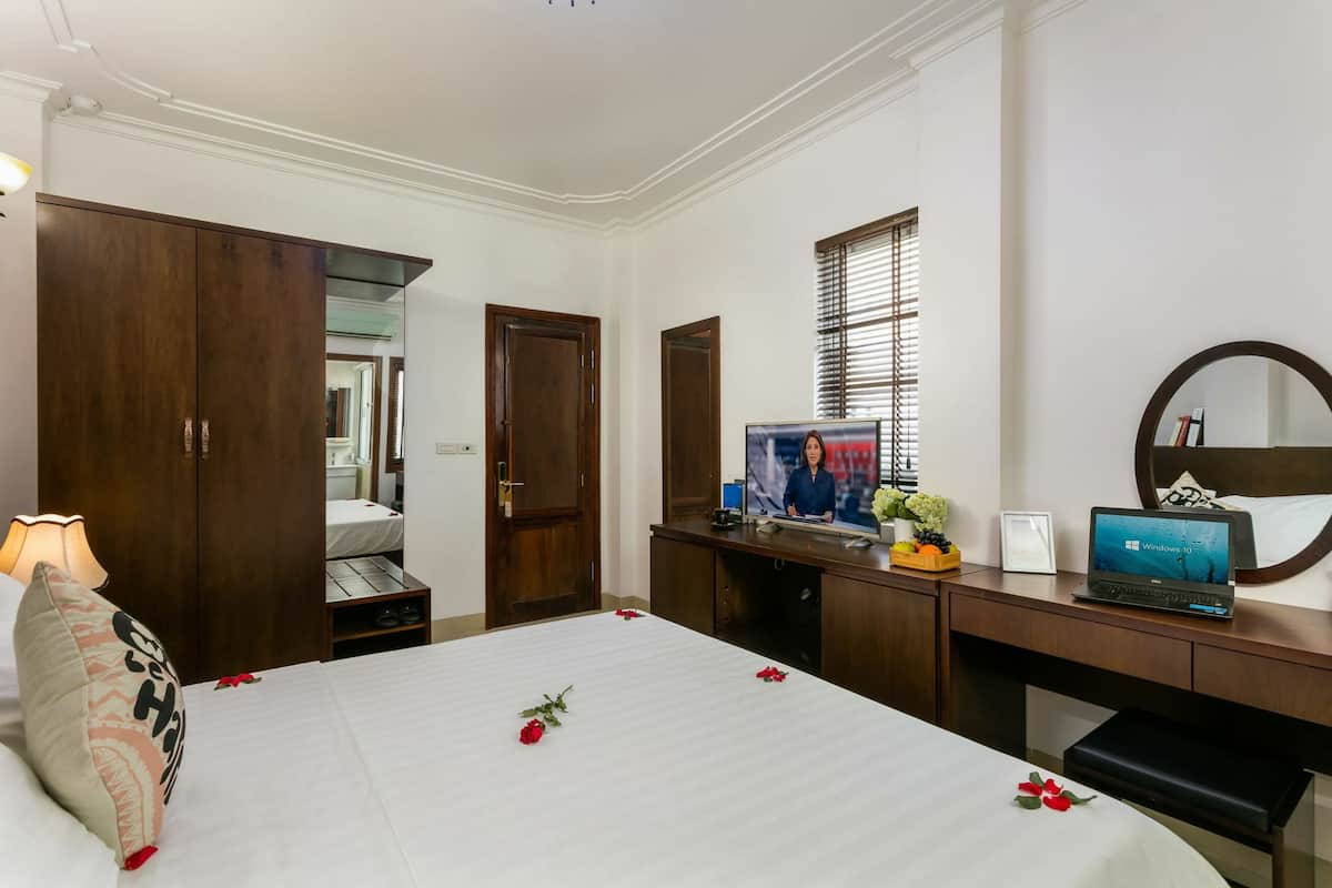 Quarto de hotel com cama, escrivaninha com laptop, televisão e guarda-roupa.
