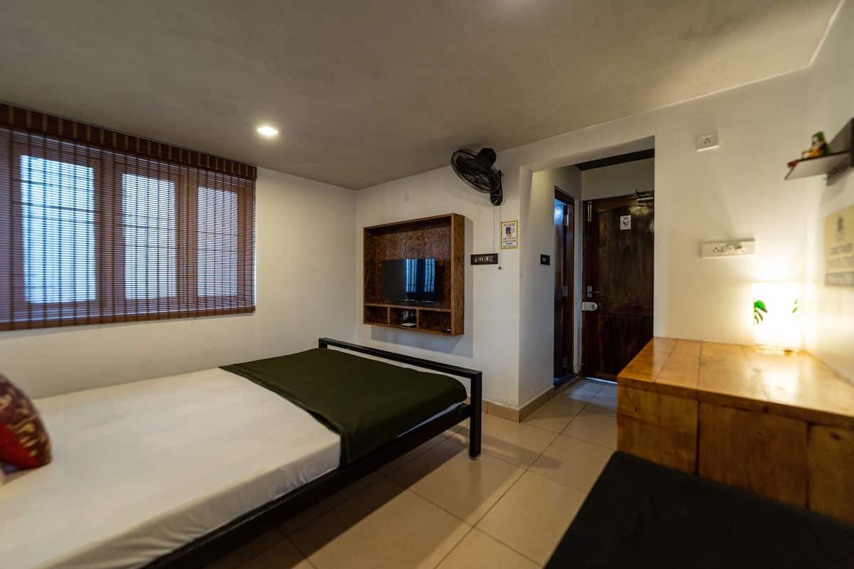 A single bed with a green blanket, a wooden cabinet, a television on the wall, and a door leading to another room.
