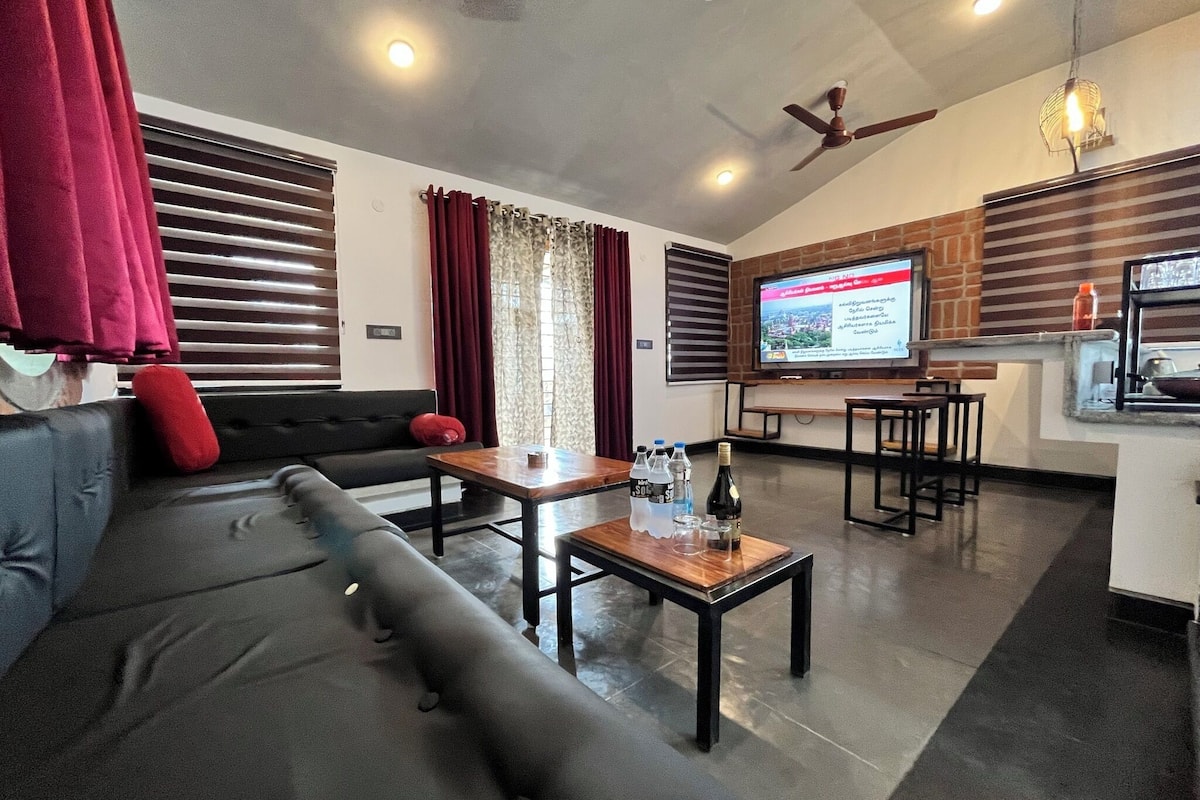 A modern living room with a sofa, a coffee table, and a TV. There is a kitchen area with a counter and stools.