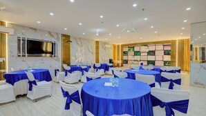 A conference room with multiple tables, white chairs with blue sashes, a large flat-screen TV, and a decorative wall with framed artwork. - BlueNeck Sec 47 near Medanta -The Medicity' Gurugram (Gurugram)
