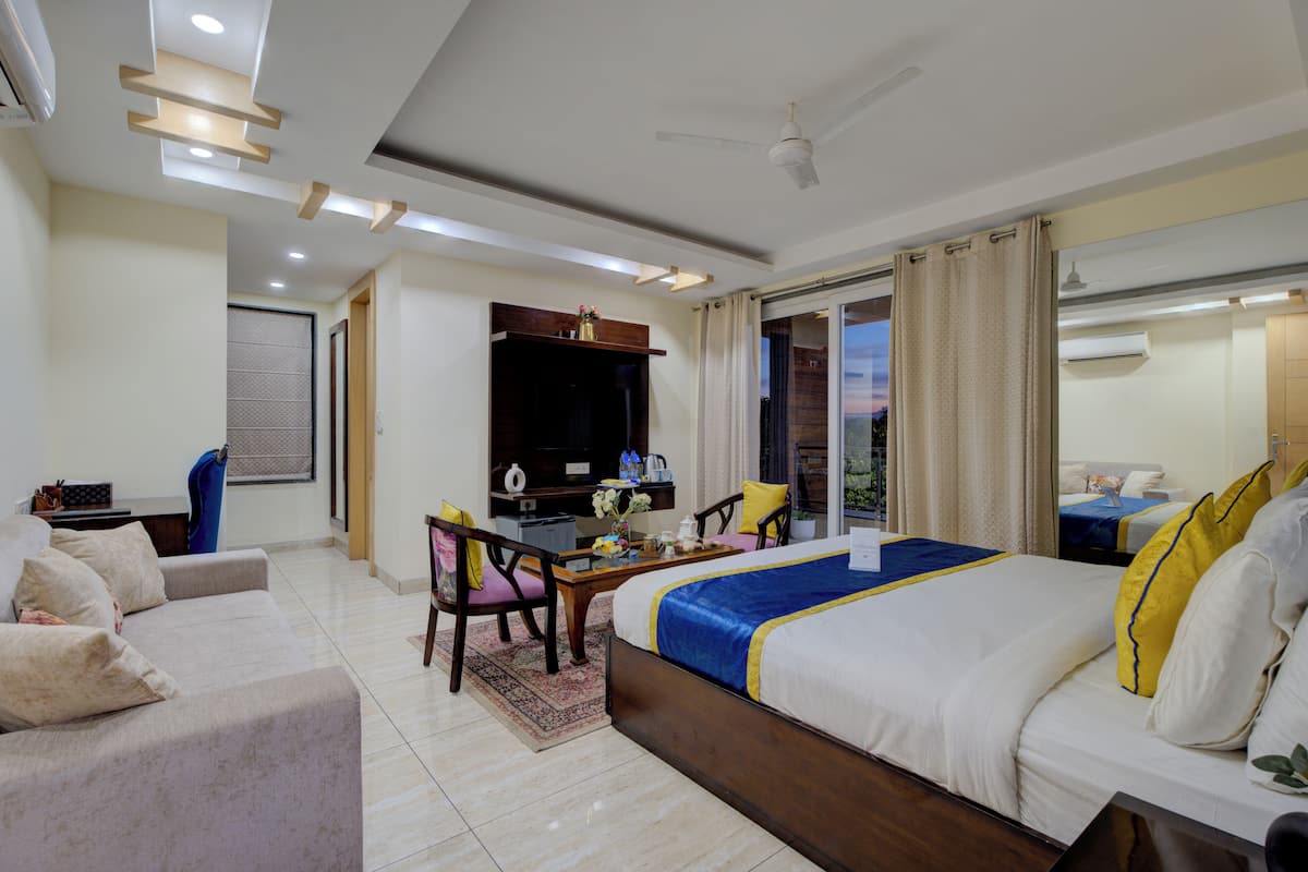 A hotel room with a large bed, a desk with a chair, a TV, and a balcony with curtains.