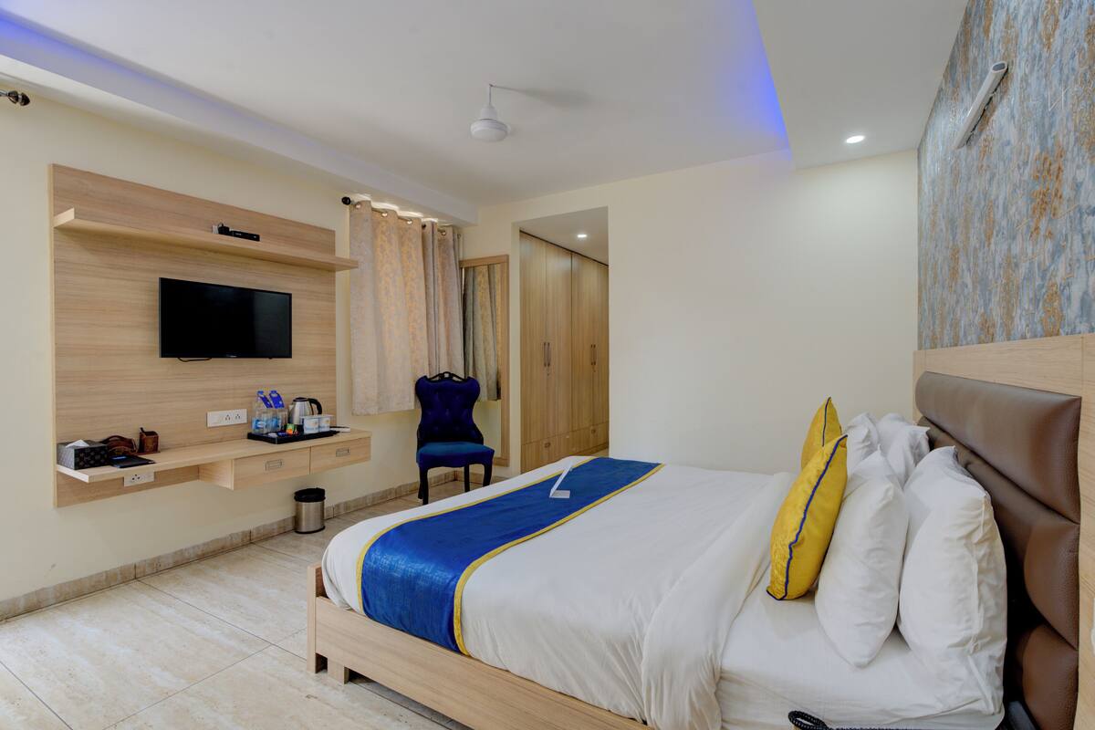 A hotel room with a bed, a TV mounted on the wall, a wardrobe, and a chair.