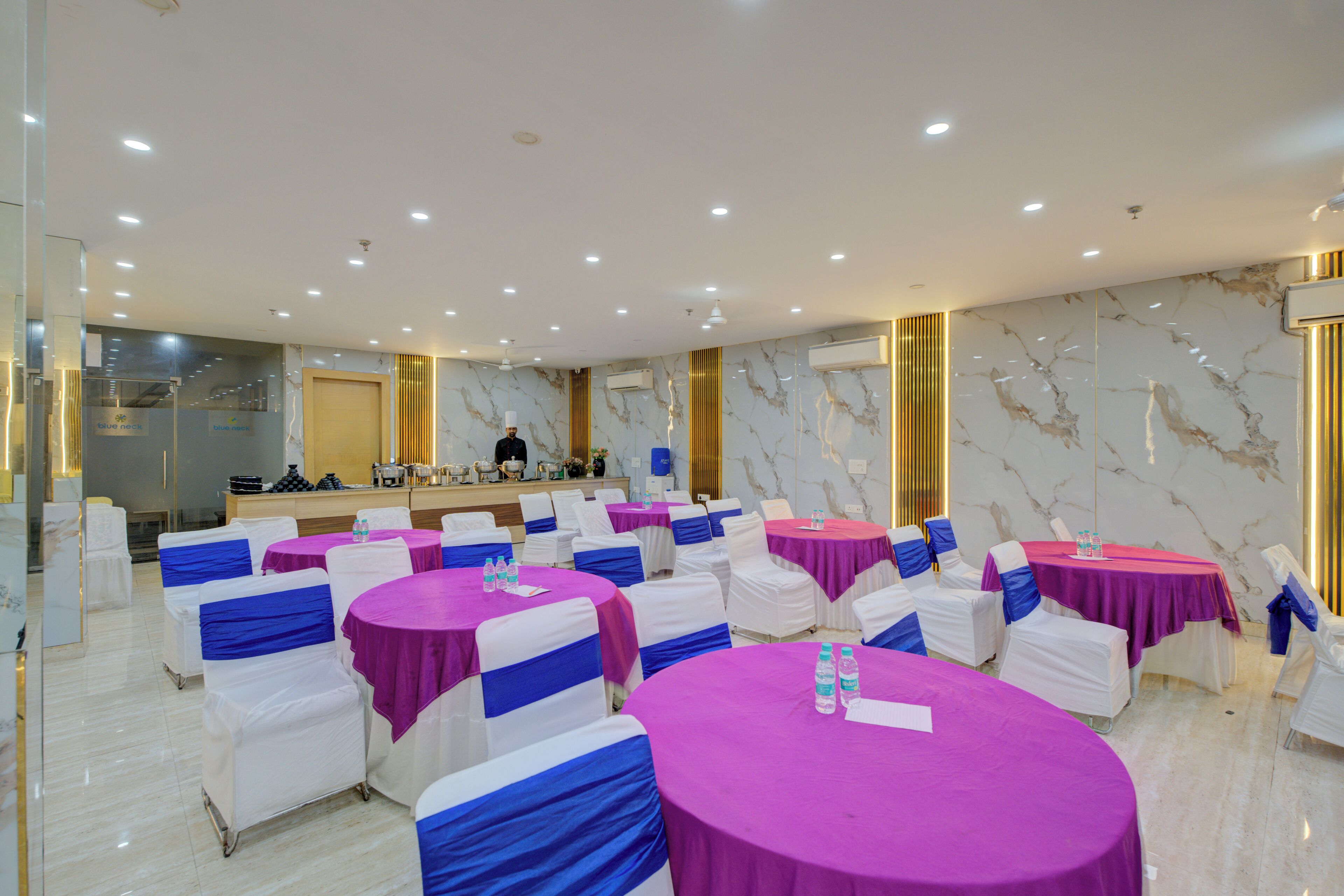 A conference room with round tables, white chairs with blue sashes, and a reception area with a counter.