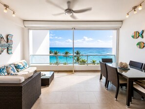 A balcony with a view of the ocean, a ceiling fan, and a dining area with wicker furniture.