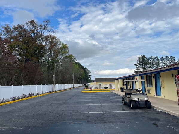 A parking lot with a golf cart, a white fence, and a building with a yellow exterior. - 712 INN (Myrtle Beach)