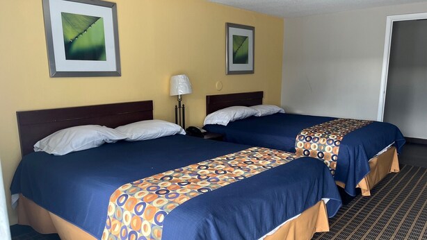 Een hotelkamer met twee bedden, elk voorzien van een geborduurde spreideken, een bedlampje en ingelijste foto's aan de muur.