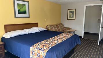 A hotel room with a bed, a nightstand, a sofa, and a door.