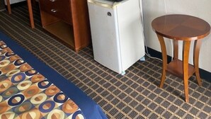 Een hotelkamer met een bed, een bureau, een koelkast, een magnetron, een televisie en een kleine ronde tafel.