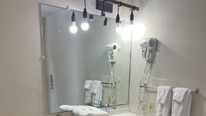 Een badkamer met een wit toilet, donker houten vloer, een wastafel met spiegel erboven en een haardroger bevestigd aan de muur.