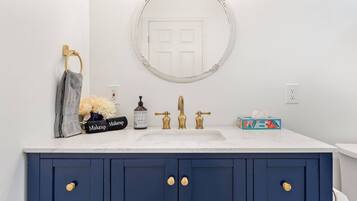 A bathroom with a white sink, gold faucets, a blue vanity with gold handles, a round mirror, and a towel rack with a gray towel.
