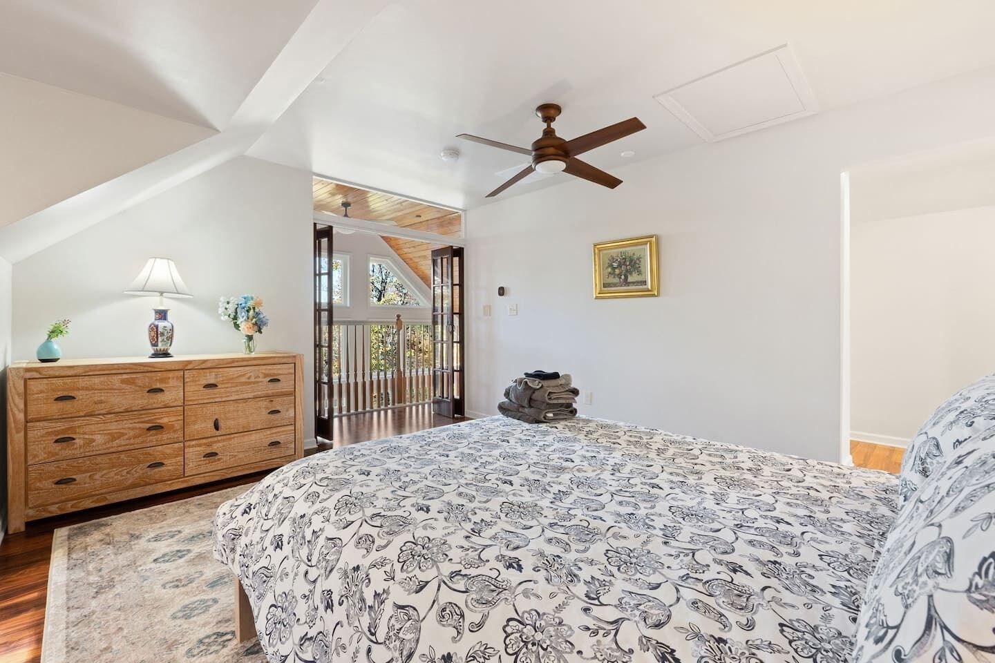 A bedroom with a large bed, a wooden dresser, a ceiling fan, and a view through a glass door.