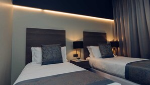 A hotel room with two beds, each with a headboard, bedside tables, lamps, and patterned pillows. - OTIA (Maputo)
