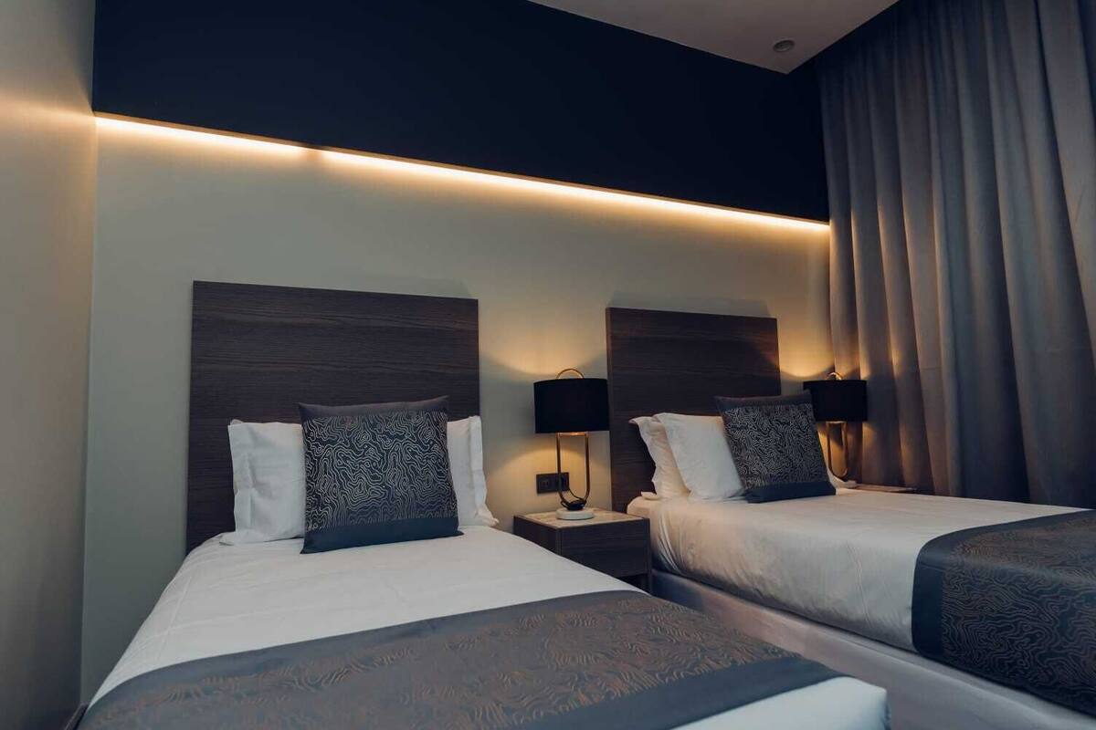 A hotel room with two beds, each with a headboard, bedside tables, lamps, and patterned pillows.