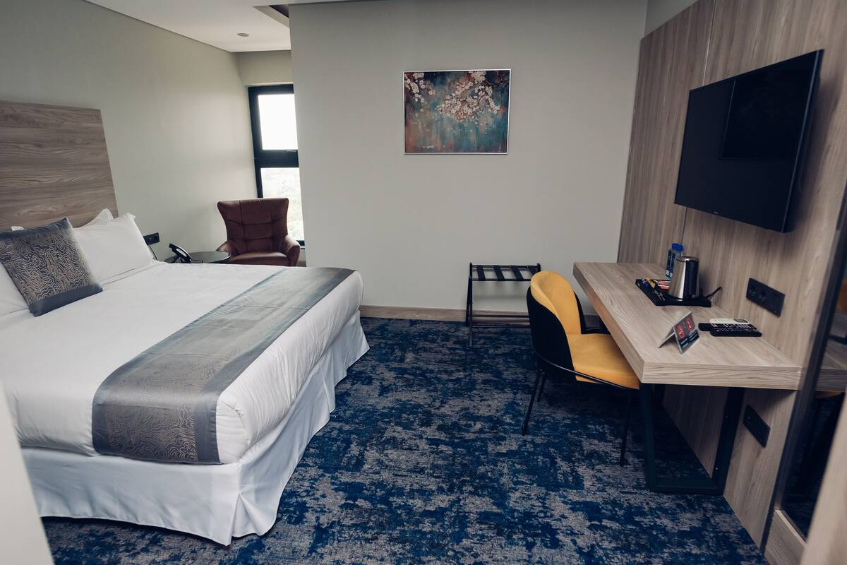 A hotel room with a large bed, a desk, a chair, a TV, and a painting on the wall.