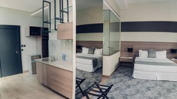 Una habitación de hotel moderna con kitchenette, dos camas, cabina de ducha de vidrio y un espejo grande.