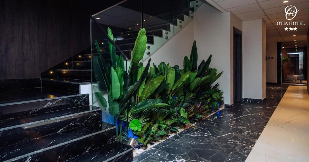 A hotel lobby with a staircase, a glass railing, and a variety of green plants.