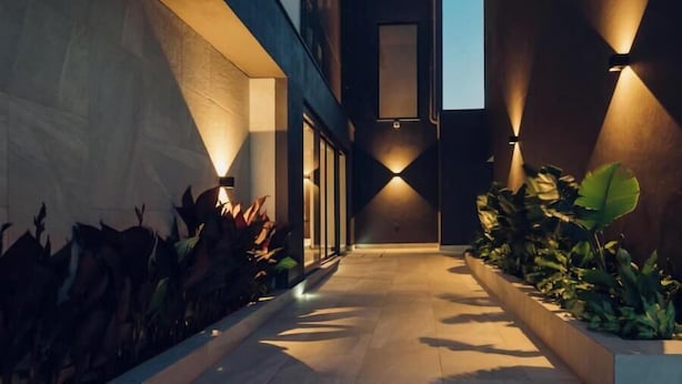 A modern building with a narrow pathway flanked by plants and illuminated by wall-mounted lights. - OTIA (Maputo)