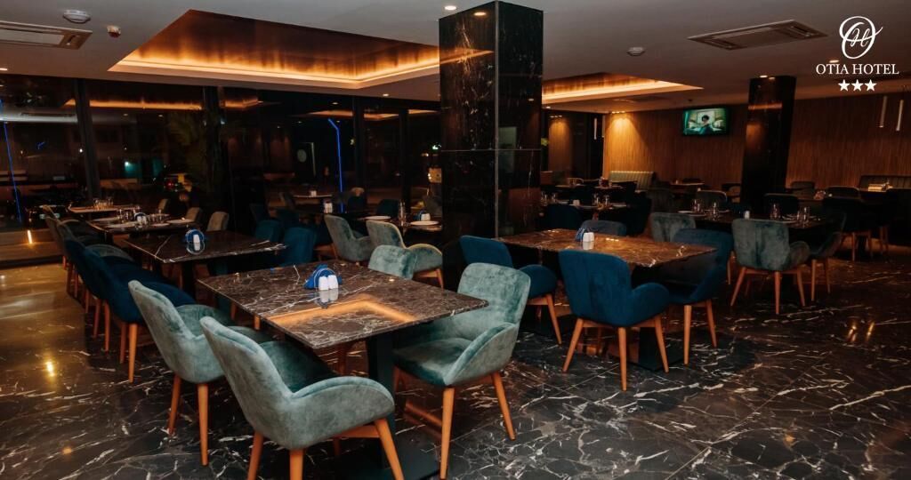 Ristorante moderno di un hotel, con pavimentazione in marmo, sedie rivestite in verde acqua e illuminazione calda e accogliente.