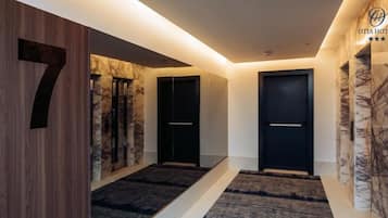 Un pasillo de hotel moderno con un revestimiento de madera, paneles de mármol y puertas negras.