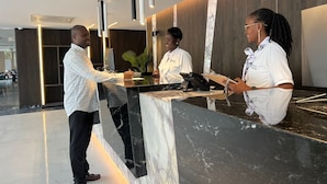 A hotel reception area with a marble counter, modern pendant lighting, and a wooden wall. - OTIA (Maputo)