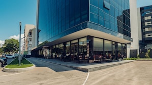 A modern building with a glass facade, outdoor seating area, and a parking lot. - OTIA (Maputo)