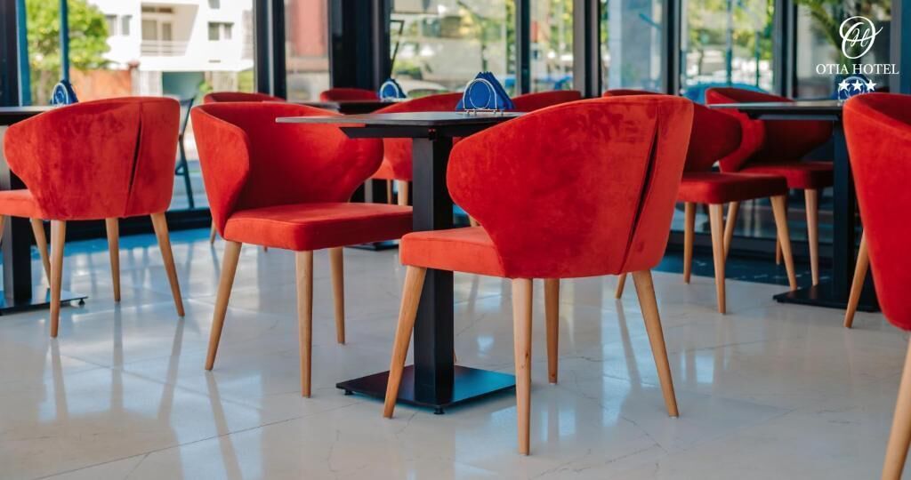 Un comedor moderno con sillas rojas y mesas negras, que cuenta con un piso de baldosas limpias y ventanas amplias.