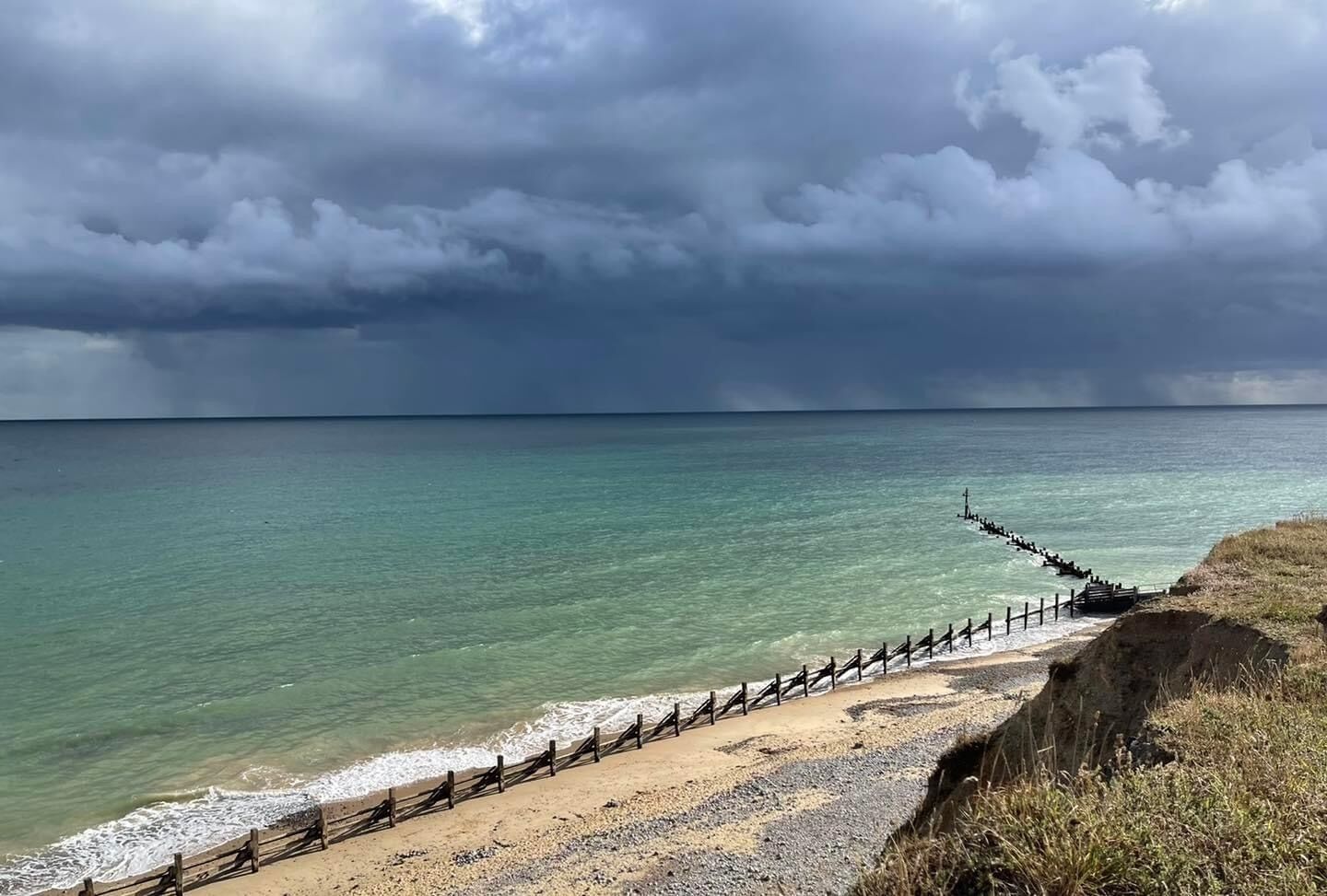A beach with a wooden walkway leading to the sea, under a cloudy sky.