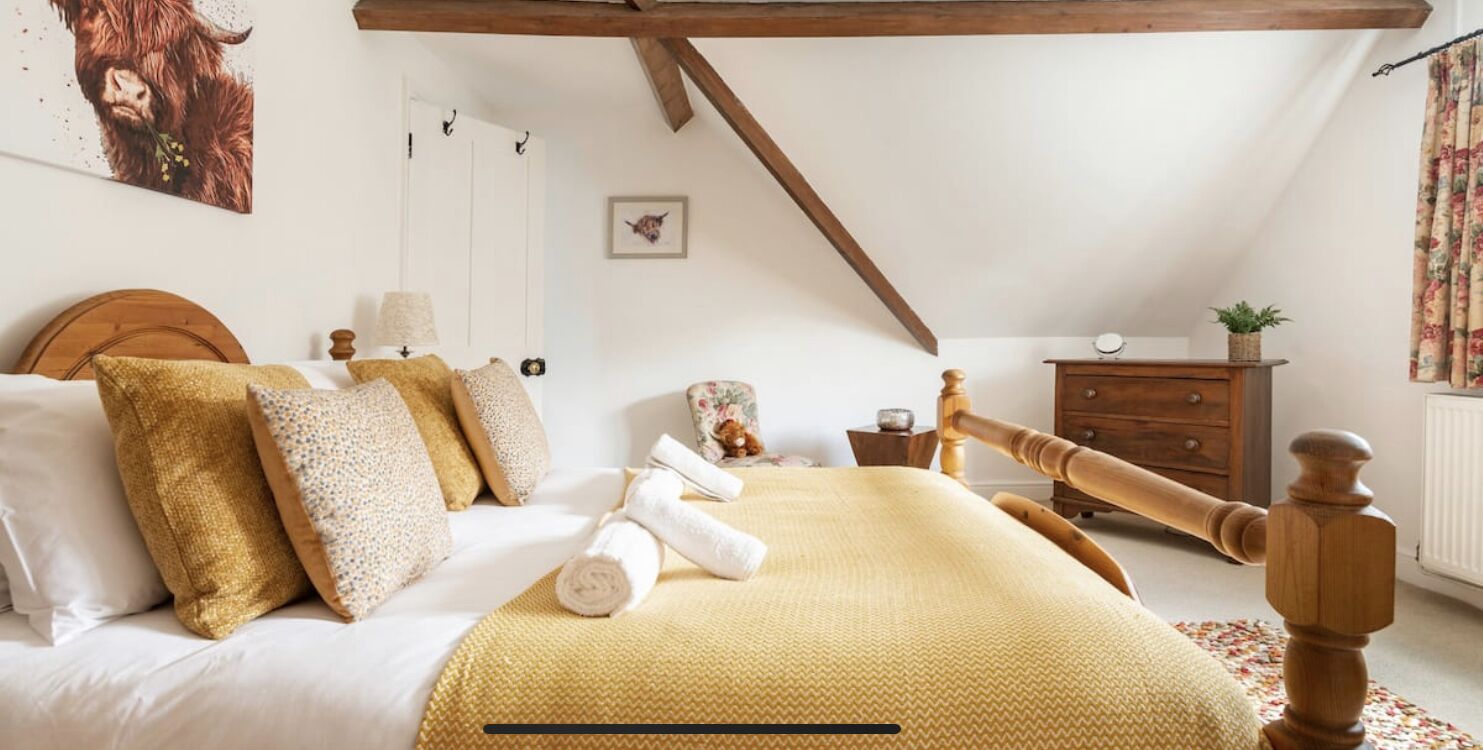 A bedroom with a bed, wooden headboard, a wooden dresser, a small table, and a picture on the wall.