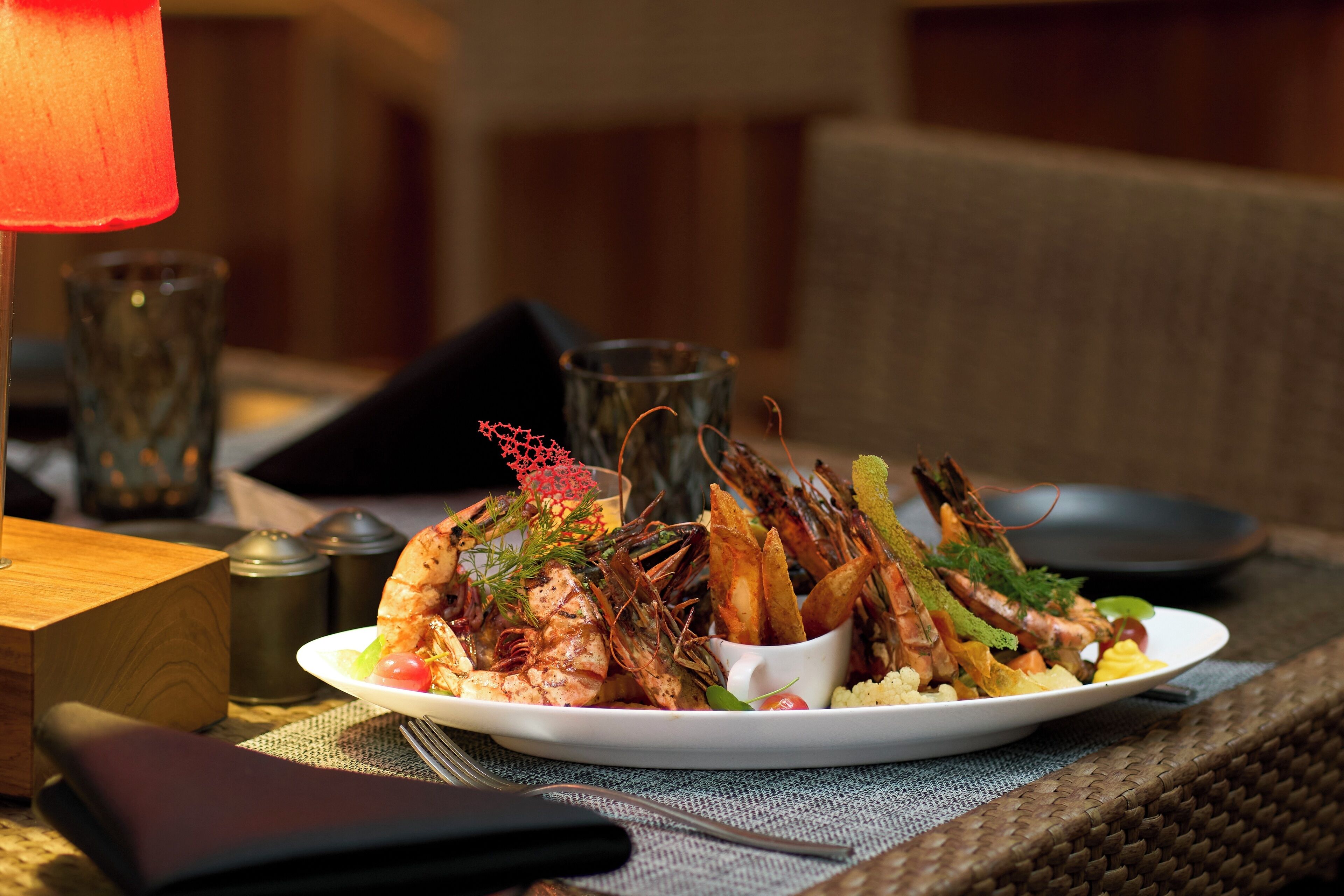 A seafood dish on a plate, a candle, and a salt shaker on a table.