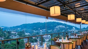 A restaurant with tables set for dining, overlooking a scenic view of a hill and cityscape.