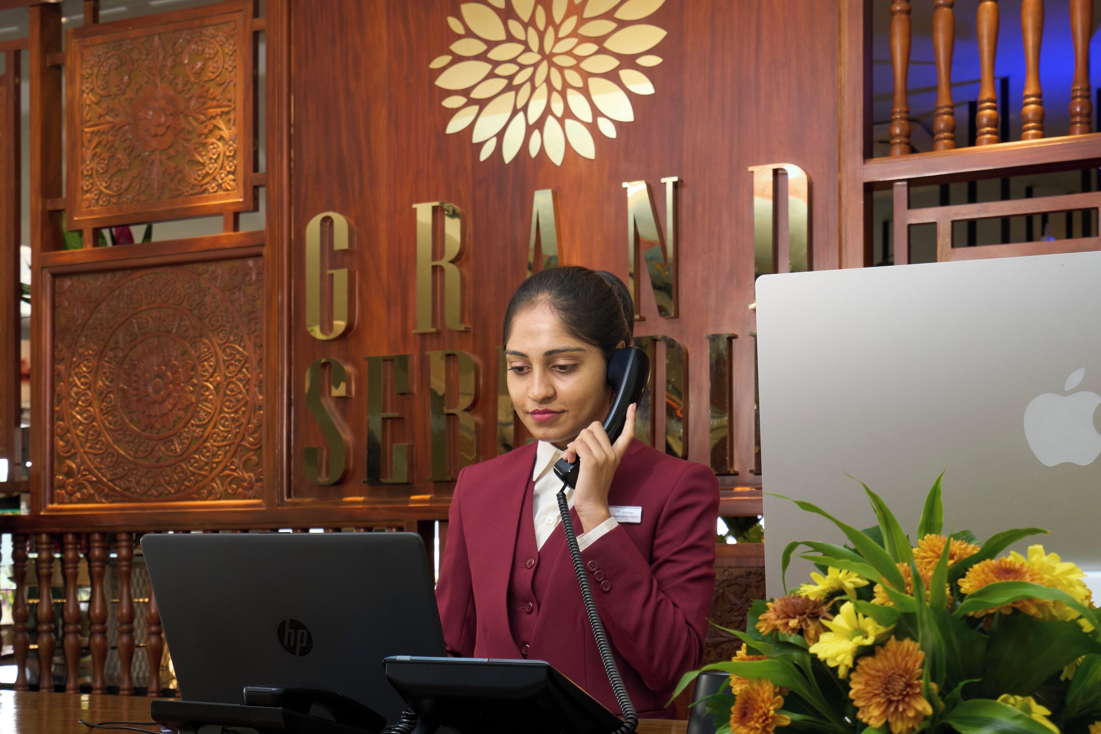 Een receptionist achter een hotel receptiebalie, met een laptop en telefoon.