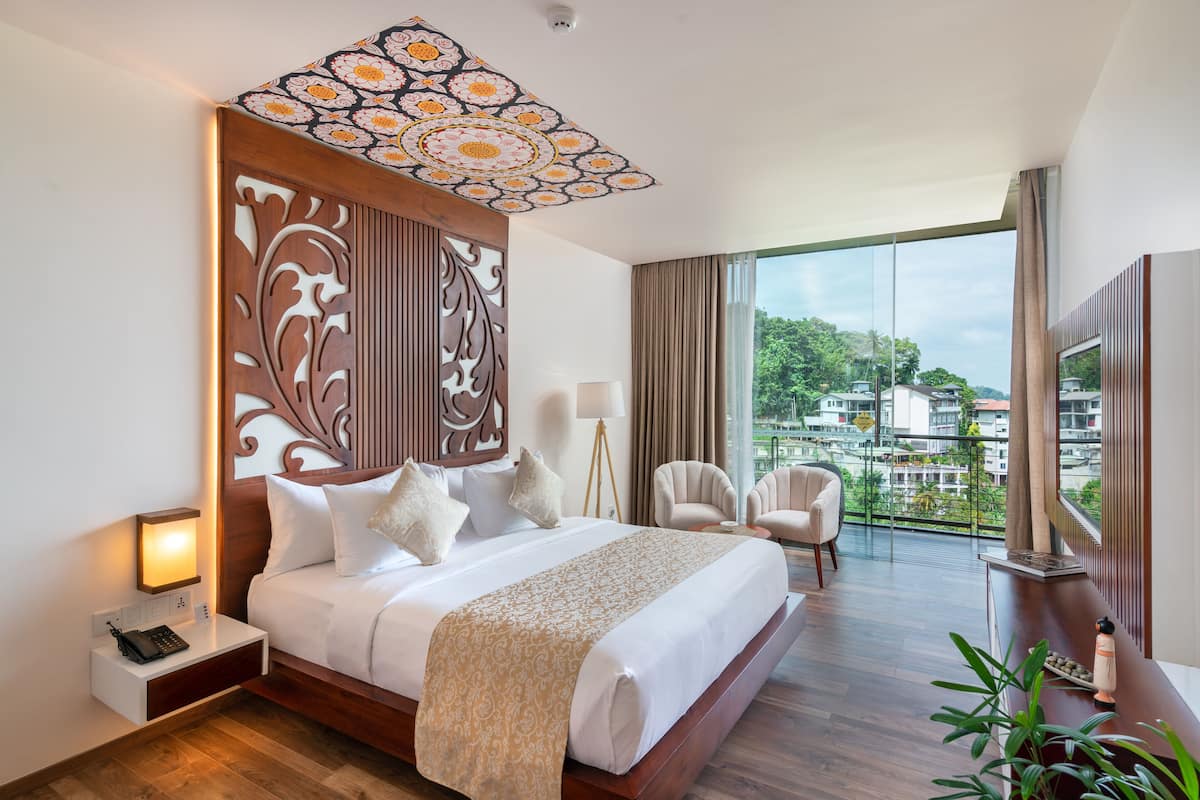 A hotel room with a large bed, a nightstand, a desk, a chair, and a large window offering a city view.