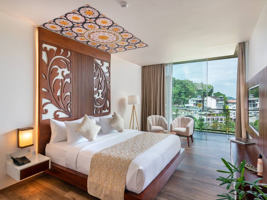 A hotel room with a large bed, a nightstand, a desk, a chair, and a large window offering a city view.