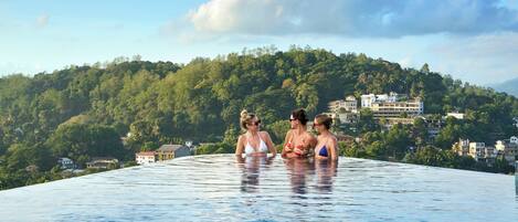 A rooftop infinity pool with a view of a lush green hillside and buildings in the background.
