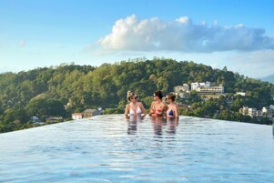 Una piscina infinita en la azotea con vistas a una colina verde y exuberante y edificios al fondo.