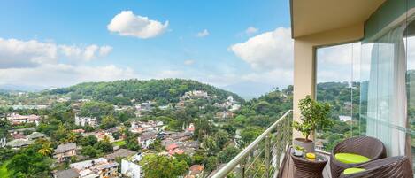Ein Balkon mit Korbmöbeln, einem Topfpflanzen und Blick auf eine Stadt mit Gebäuden und Grünflächen.