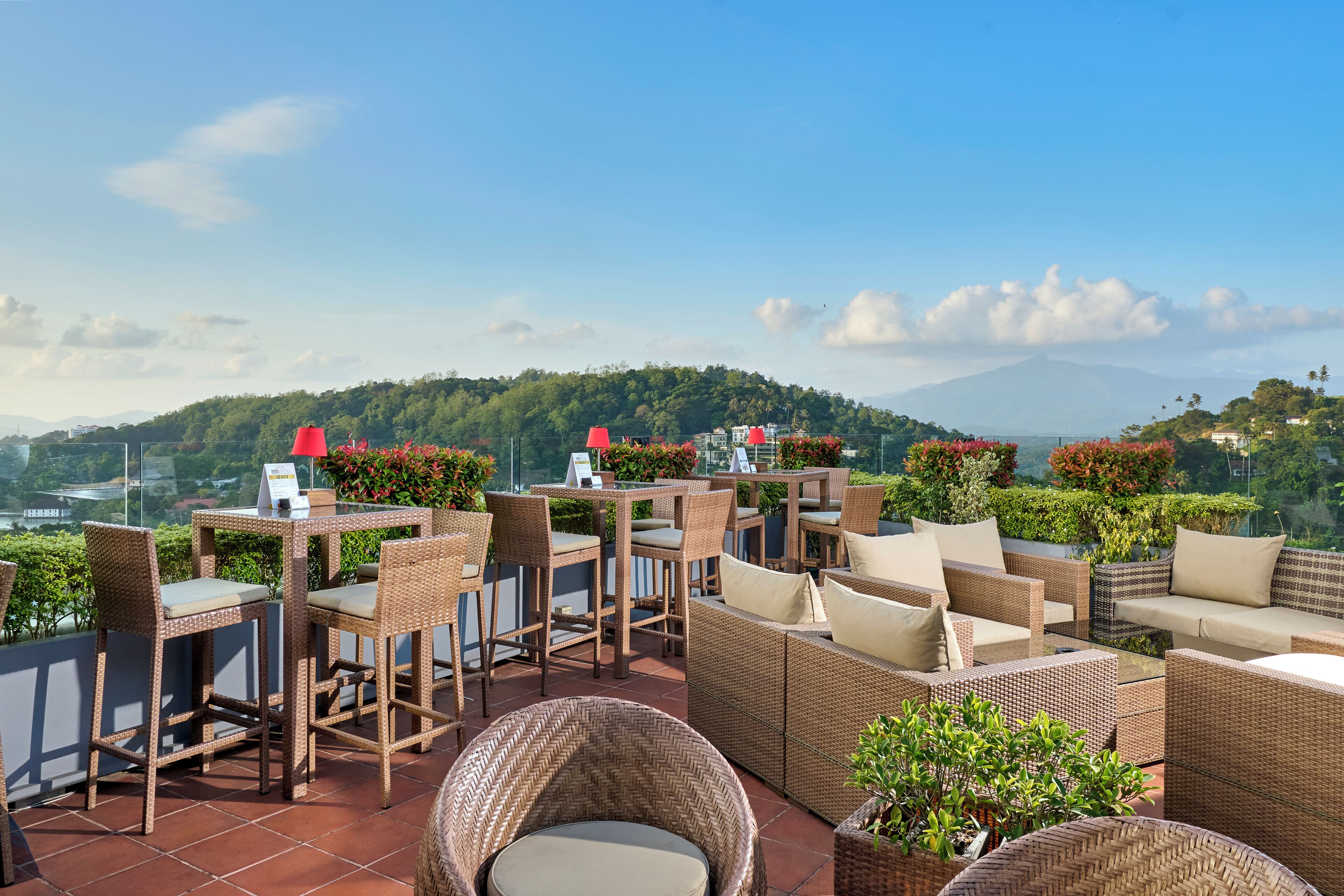 An outdoor patio with wicker furniture, tables, and chairs, overlooking a lush green landscape and a mountain in the distance.
