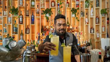 A bartender holding two drinks at a bar with shelves of liquor bottles in the background.
