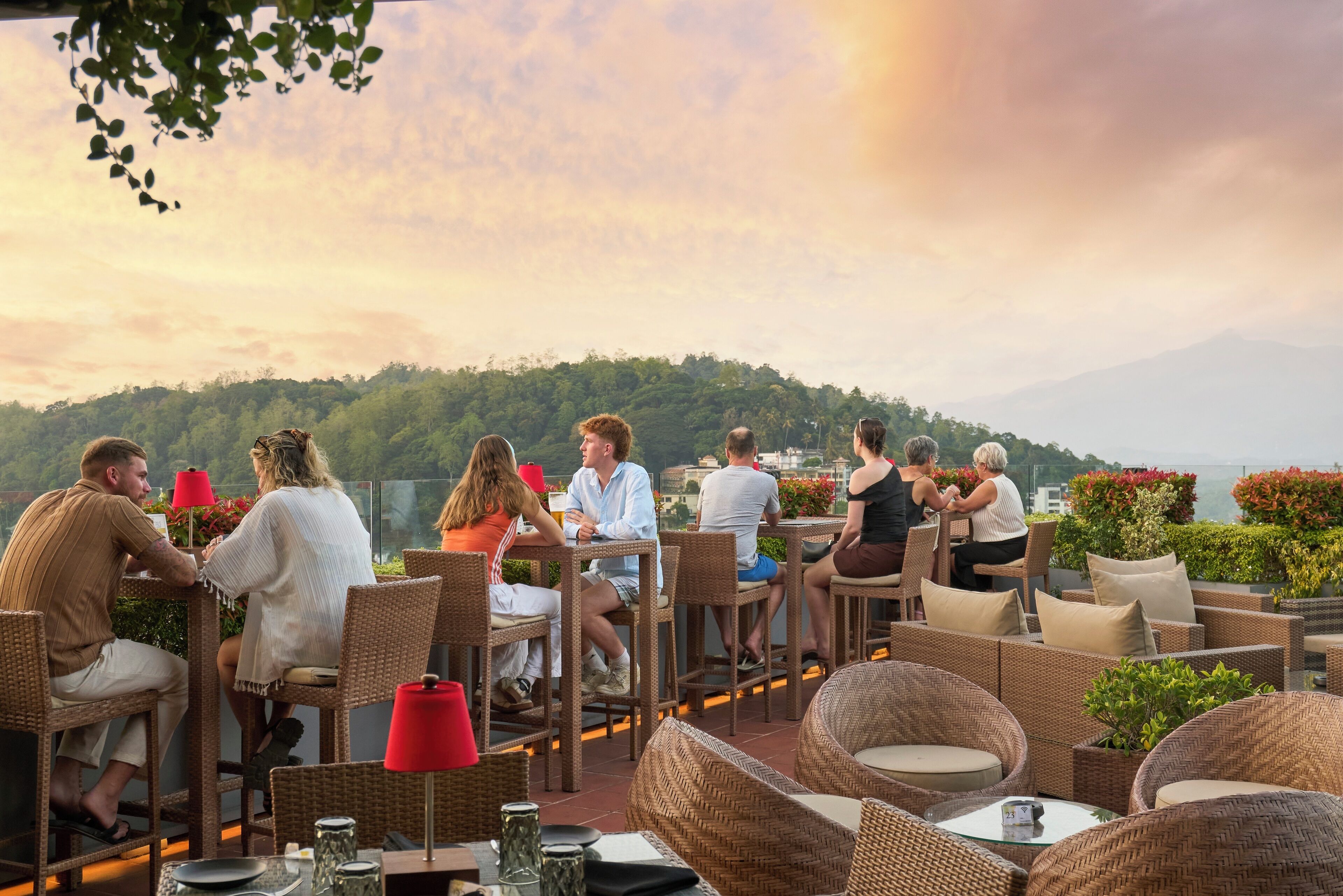 A rooftop dining area with wicker furniture and a view of a forested hill.