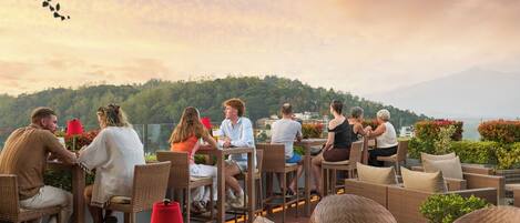 A rooftop dining area with wicker furniture and a view of a forested hill.