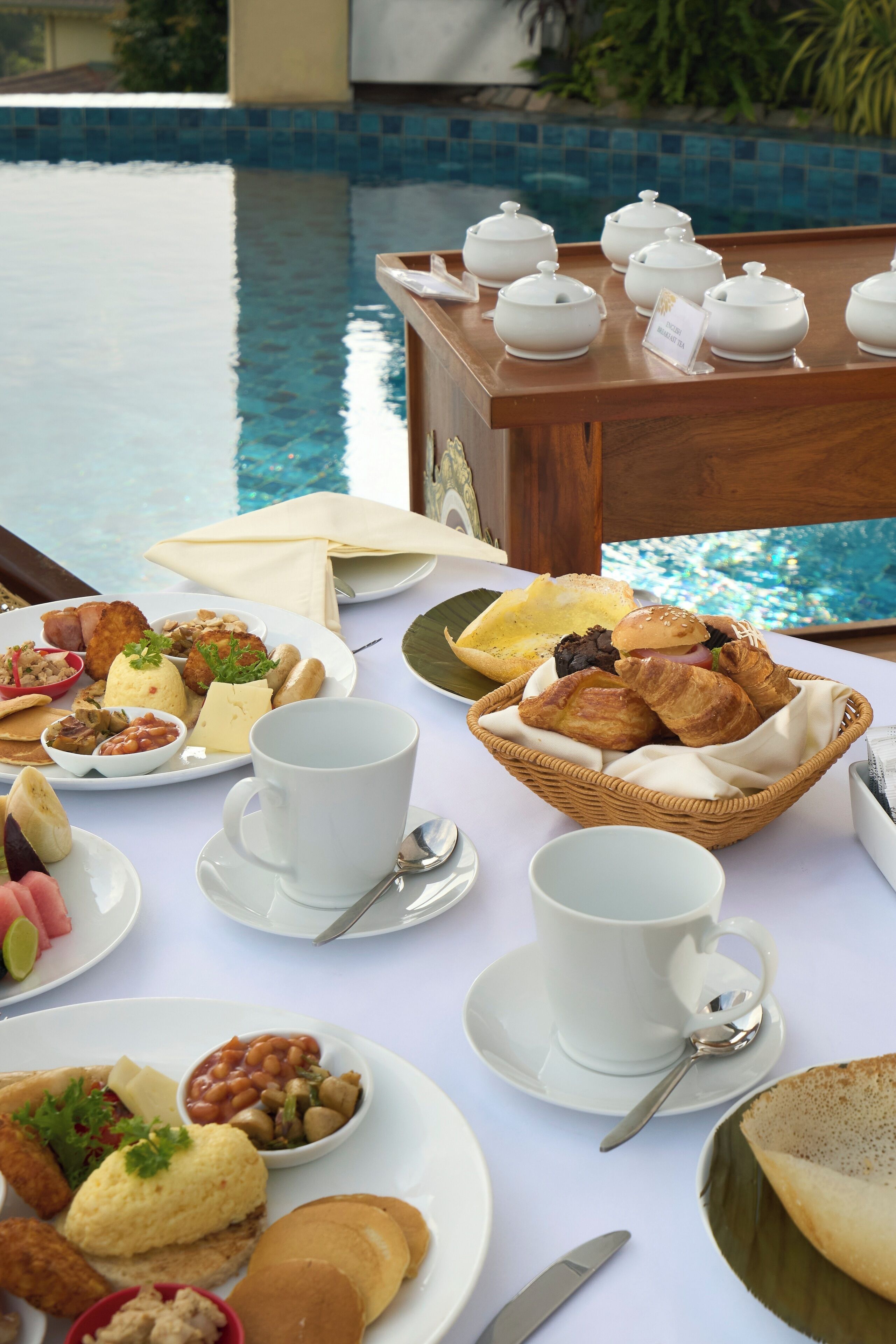 A breakfast buffet with various dishes and beverages by a poolside.