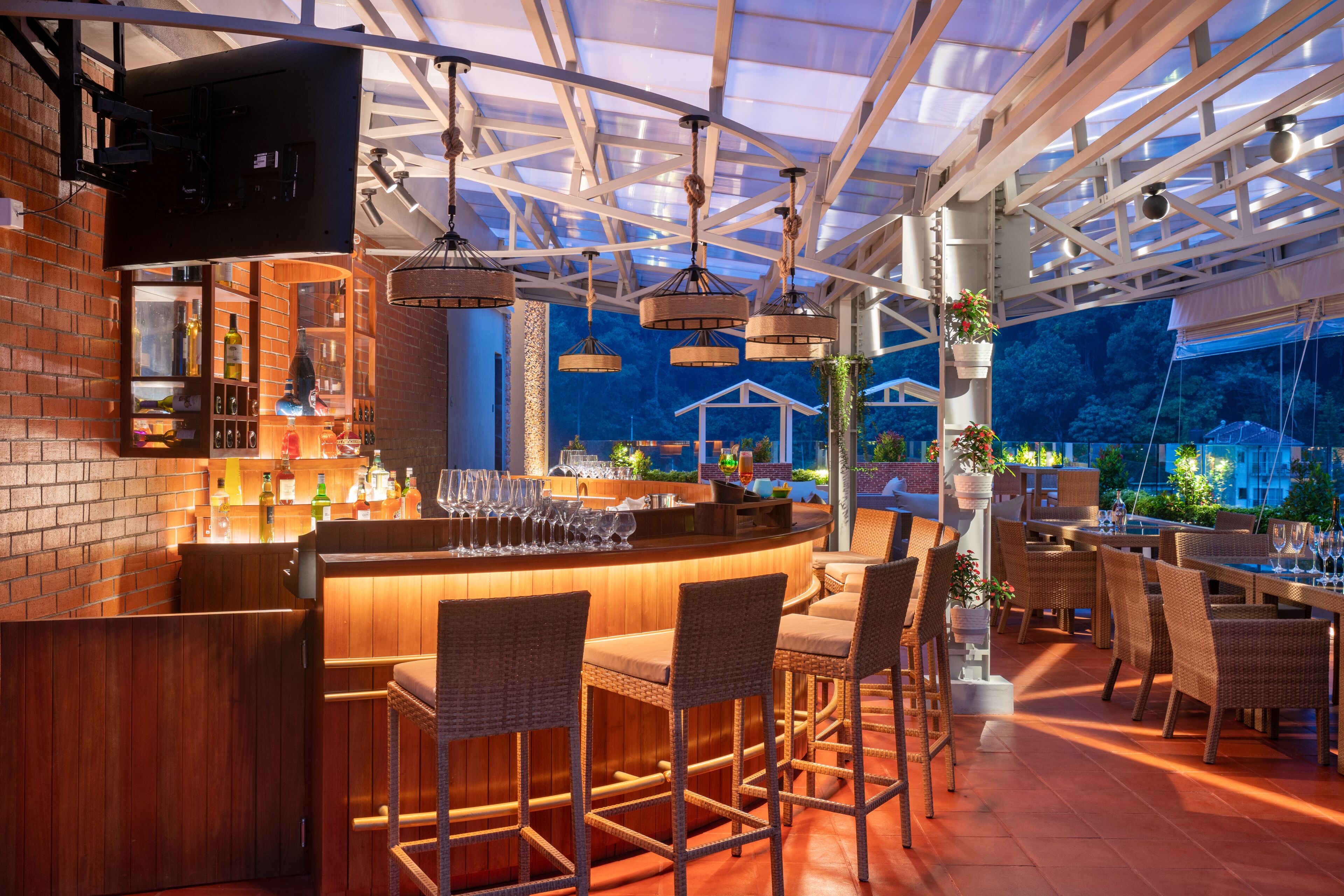 An outdoor bar area with a brick wall, wooden bar counter, and wicker chairs.
