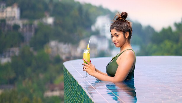 A person relaxing by a pool with a drink, overlooking a scenic landscape.