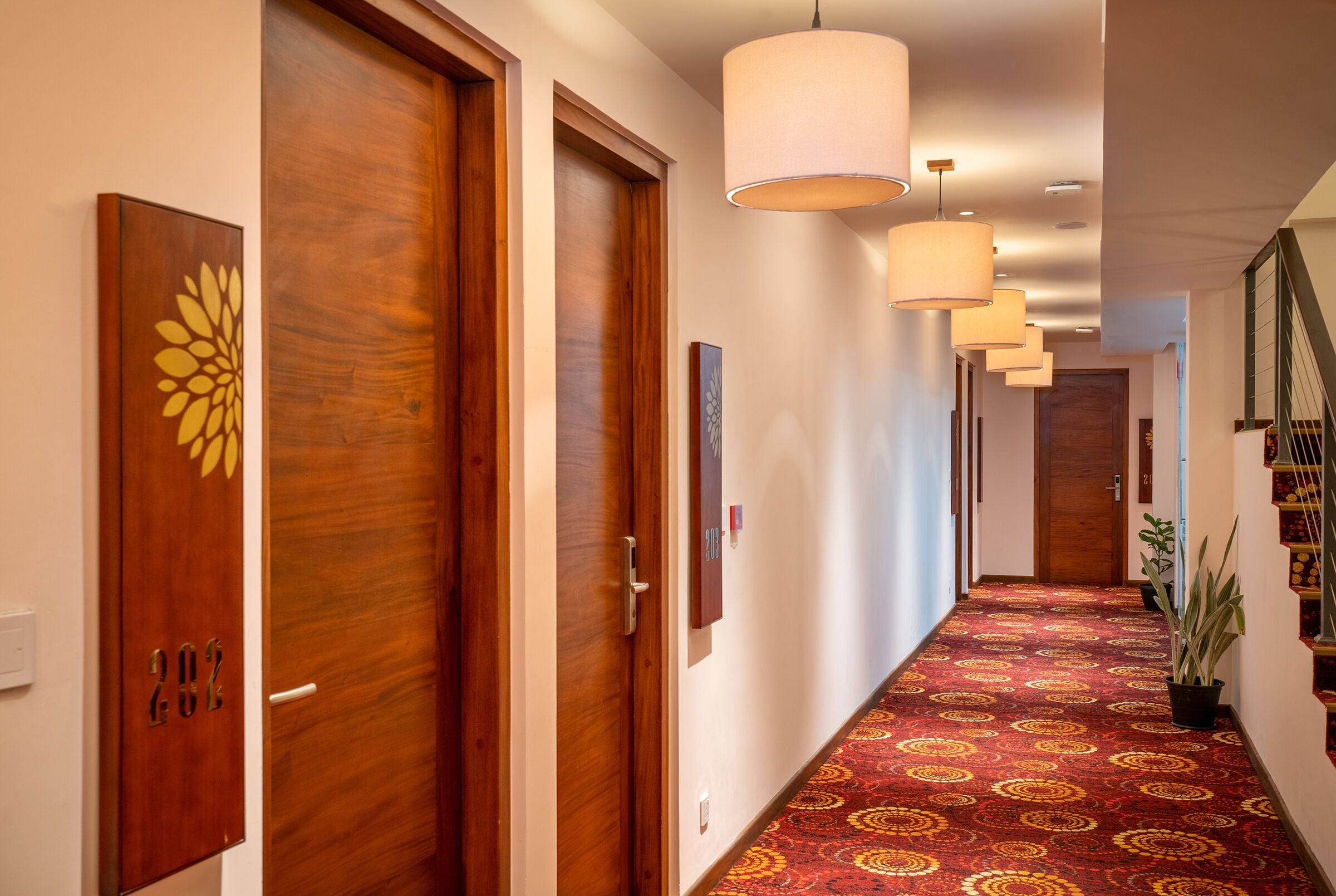 Un couloir d’hôtel avec des portes en bois, une moquette à motifs et des luminaires suspendus.