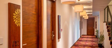 A hotel hallway with wooden doors, a patterned carpet, and pendant lighting.