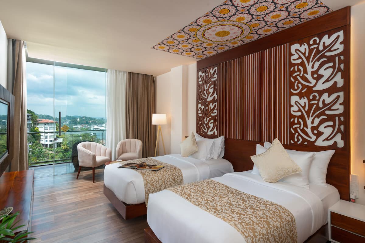 A hotel room with two beds, a large window with a view, a ceiling with a decorative pattern, and a wooden headboard with a carved design.