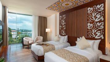 A hotel room with two beds, a large window with a view, a ceiling with a decorative pattern, and a wooden headboard with a carved design.