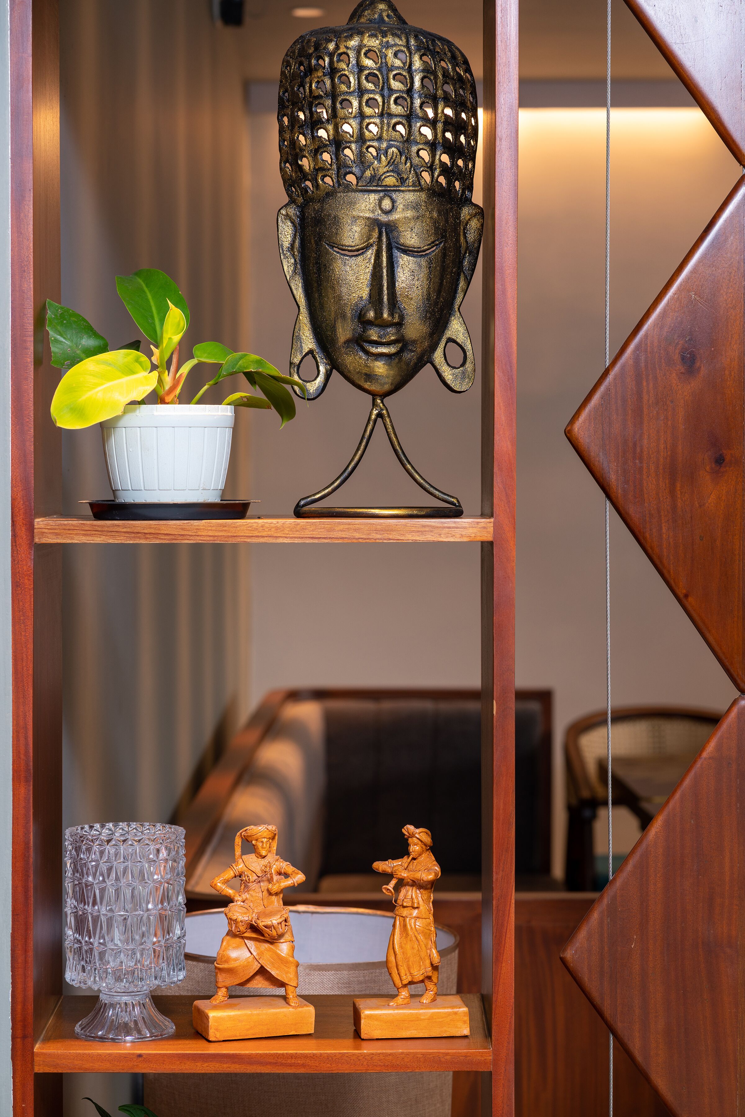A shelf with a Buddha head sculpture, a potted plant, a glass vase, and two wooden figurines.