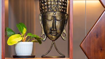 A shelf with a Buddha head sculpture, a potted plant, a glass vase, and two wooden figurines.